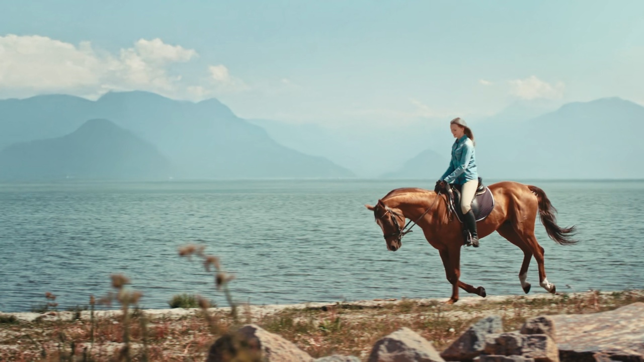 Une cavalière à cheval près de l’eau, avec un paysage montagneux intégré à l’aide d’effets visuels.